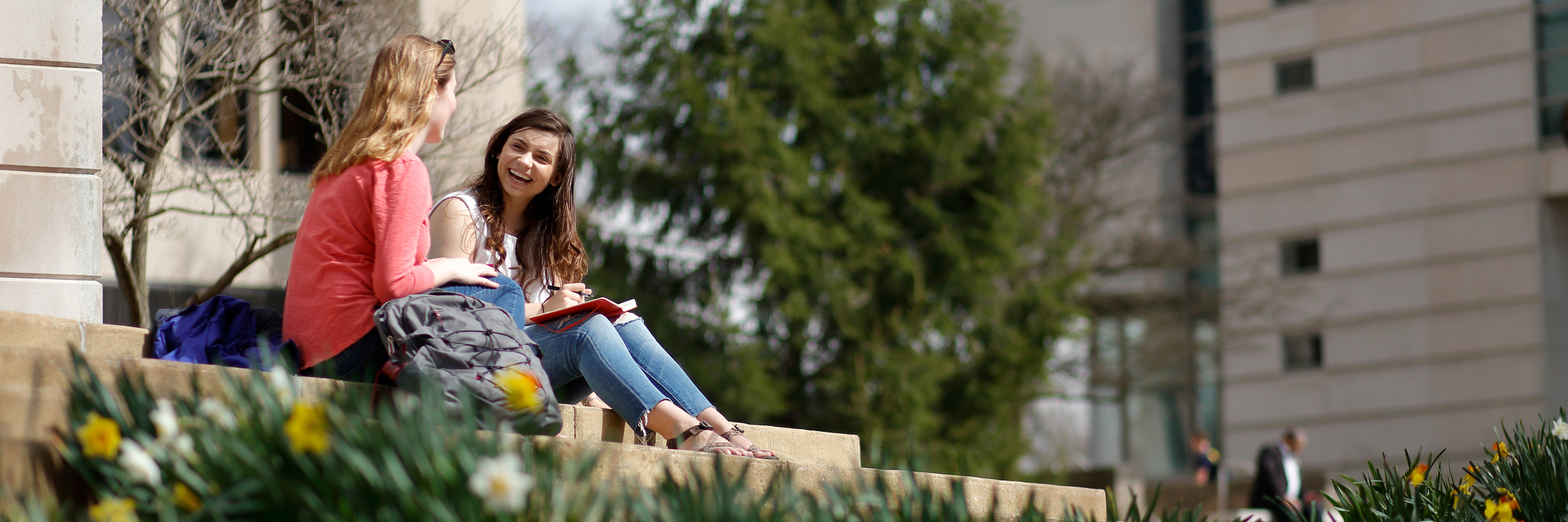 Two Indiana University students sit outside on the Indiana University Bloomington campus and talk.