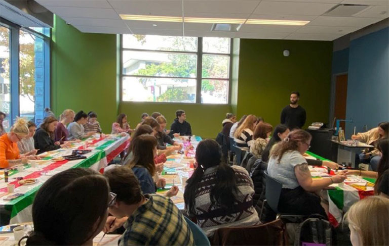 A crowded classroom, where students construct crafts at several long tables.