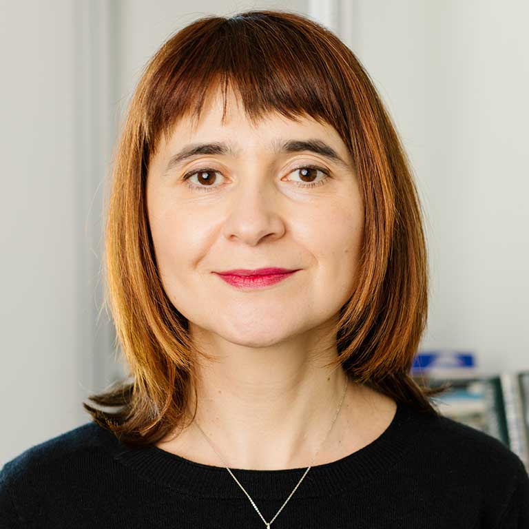 A headshot of Oana Panaite, who wears a black shirt and poses against a white background.