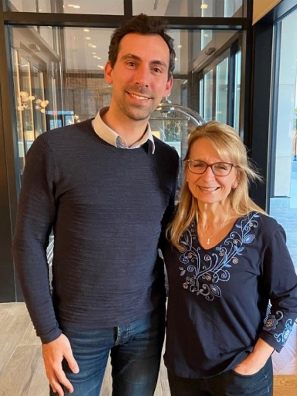 Two people pose together with a glass entryway in the background.
